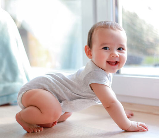 Raczkowanie – uśmiechnięte niemowlę na drewnianej podłodze w domu