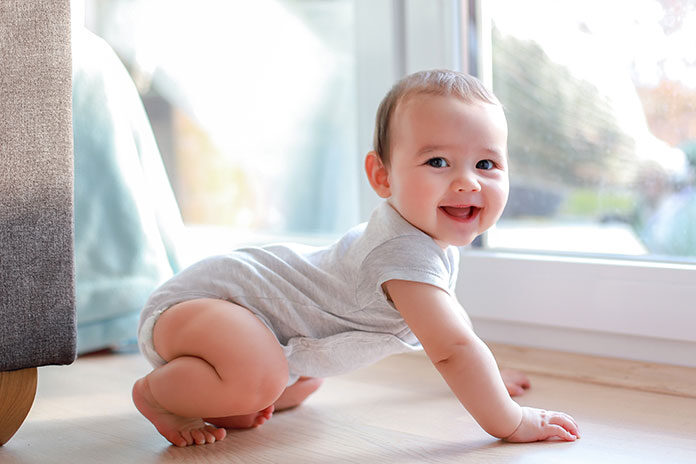 Raczkowanie – uśmiechnięte niemowlę na drewnianej podłodze w domu
